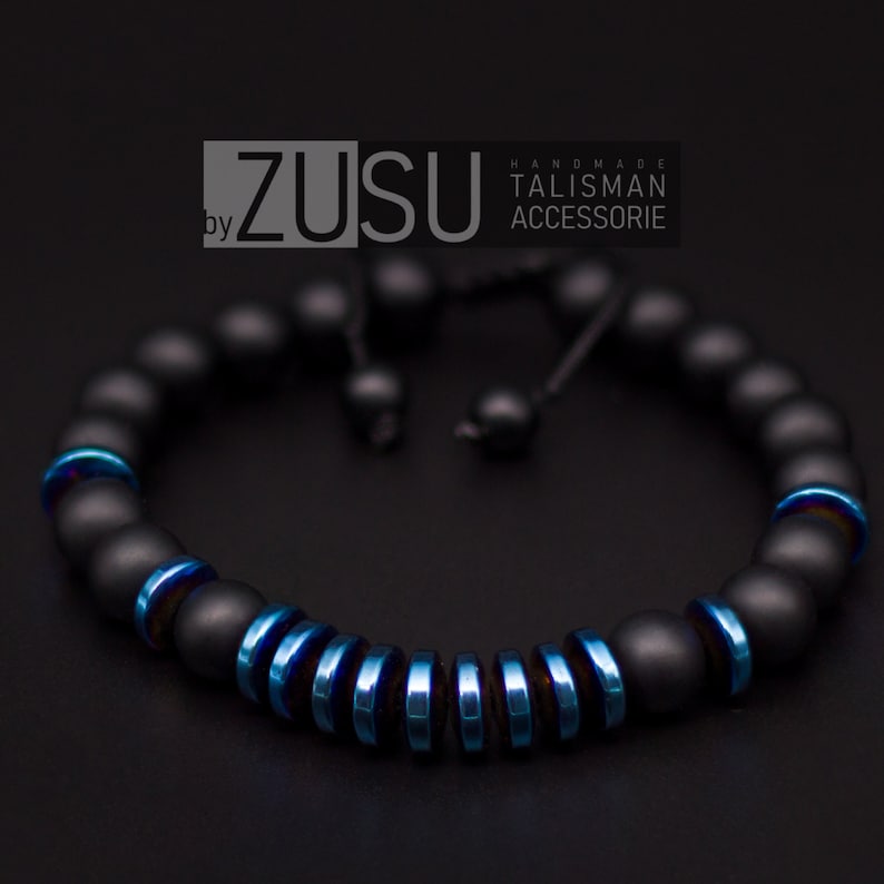 May include: Black beaded bracelet with a blue metal accent. The bracelet is adjustable with a black cord. The text "by ZUSU HANDMADE TALISMAN ACCESSORIE" is visible in the image.