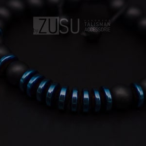 May include: A black and blue beaded bracelet with the text "ZUSU by HANDMADE TALISMAN ACCESSORIE".