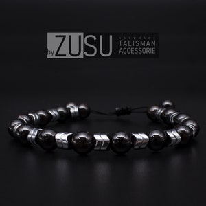 Könnte beinhalten: Schwarzes Perlenarmband mit silbernen Akzenten. Das Armband besteht aus schwarzen Perlen und silbernen Abstandshaltern. Das Armband ist mit einer schwarzen Schnur gebunden.
