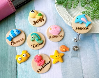 May include: A set of eight wooden badge reels with various sea creature designs and names, including Jess, Taylor, Oceane, Rebecca, Christine, Jessica, and a starfish.