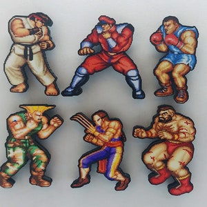 Può includere: Sei figurine in stile pixel art di personaggi della serie di videogiochi Street Fighter. I personaggi sono Ryu, Ken, Sagat, Guile, Zangief e Chun-Li. Le figurine sono in legno e sono dipinte con colori vivaci.