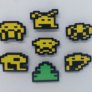 May include: Seven pixel art style magnets, featuring a green tree, and six yellow and black space invaders. The space invaders have different expressions and poses.