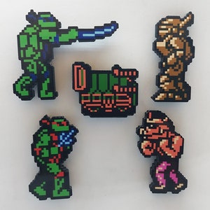 May include: Five pixel art style character figures, including a green turtle with a blue weapon, a green vehicle, a brown armoured figure, a red and pink figure, and a green turtle with a blue weapon.