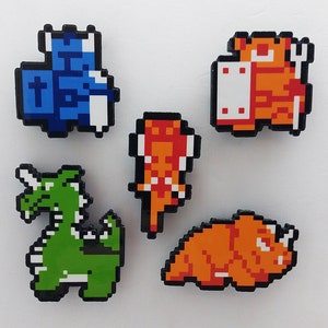 May include: Five pixel art style pins featuring a blue and white castle, a red and white dragon, a green and white dragon, an orange and white fish, and an orange and white worm.