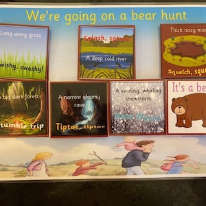 May include: A children's game board with illustrations and text. The game features cards with phrases like "Long wavy grass" and "It's a bear!" with corresponding images. The title "We're going on a bear hunt" is at the top of the board.