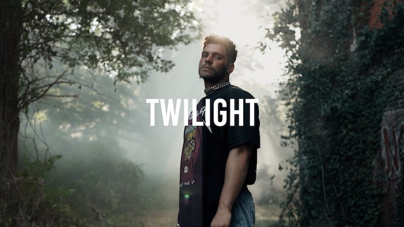 May include: A man wearing a black t-shirt with a graphic print and blue jeans stands in a foggy forest. The text "TWILIGHT" is written in white letters on a black background.
