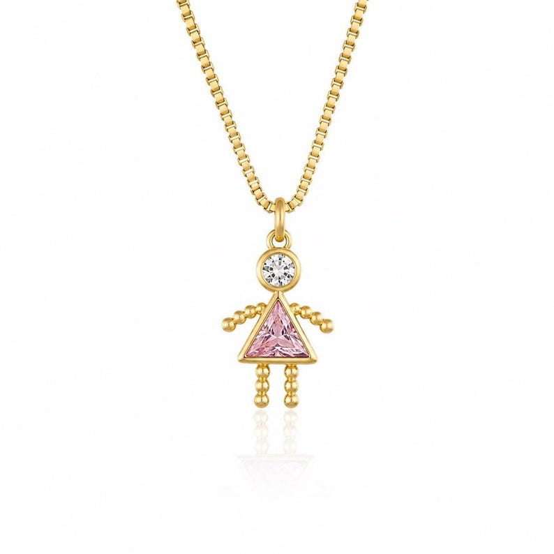 May include: A gold-toned necklace featuring a pendant shaped like a stylized figure. The head is a round clear stone, while the triangular body is a faceted pink stone. The arms and legs are made of small gold beads on a delicate box chain.