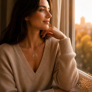 May include: A gold-toned necklace featuring three small, dangling charms shaped like stylized figures. Each charm is accented with a different colored gemstone, including purple, green, and orange, suspended from a delicate gold-colored chain.