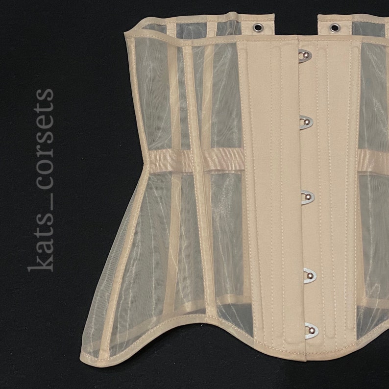 May include: A beige corset with a sheer mesh and silver metal busk