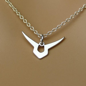 May include: A silver-colored pendant necklace featuring a stylized, symmetrical design with wing-like extensions. The pendant hangs from a delicate chain, creating a minimalist and elegant aesthetic. The necklace is displayed against a neutral background.