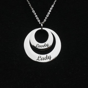 May include: A silver necklace with a double circle pendant. The larger circle has the word "Lady" engraved on it, and the smaller circle has the word "Lovely" engraved on it.