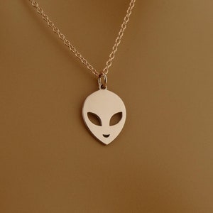 Peut inclure: Un collier en chaîne dorée avec un pendentif en forme de tête d'extraterrestre. Le pendentif est découpé, de sorte que le visage de l'extraterrestre est visible.