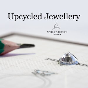 Könnte beinhalten: Nahaufnahme eines klaren Diamanten auf einem weißen Blatt Papier mit einem Bleistift und einer Ringzeichnung. Das Papier trägt den Text "Upcycled Jewellery" und "Apsley & Heron London".