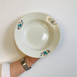 May include: A white ceramic soup bowl with a floral design in shades of blue, green, and red. The bowl has a slightly raised rim and a smooth, glossy finish.