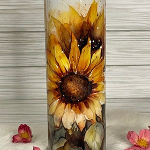 May include: A stainless steel tumbler with a watercolor design of sunflowers. The tumbler has a white background with brown and yellow sunflowers.