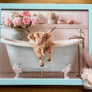 May include: A Highland cow taking a bath in a vintage clawfoot tub with pink flowers in the background. The tub is light blue and has white feet. The cow is brown and white and has a fluffy coat.