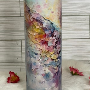 May include: A tall, insulated tumbler with a colorful, abstract watercolor design. The design features a blend of pastel colors, including pink, blue, yellow, and purple, creating a textured, artistic appearance. The tumbler has a clear lid and is suitable for cold beverages.