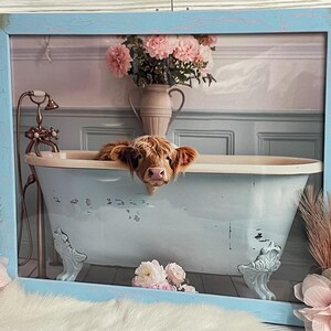 May include: A Highland cow peeks over the edge of a light blue clawfoot bathtub with a white interior. The bathtub is in a bathroom with a pink and white floral arrangement in a vase.