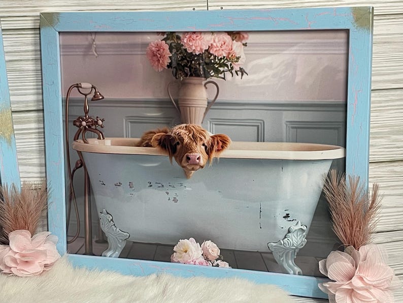 May include: A Highland cow peeks over the edge of a light blue clawfoot bathtub with a white interior. The bathtub is in a bathroom with a pink and white floral arrangement in a vase.