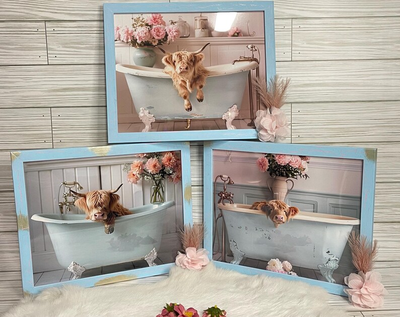 May include: Three framed prints of Highland cows in a bathtub. Each print features a different cow in a light blue bathtub with floral accents. The frames are light blue with gold accents.