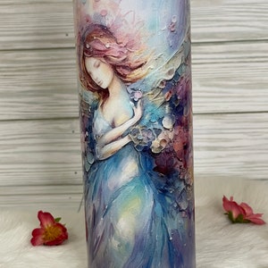 May include: A stainless steel tumbler featuring a watercolor illustration of a woman with flowing hair and a flowing gown. The design incorporates soft blues, purples, and pinks. The tumbler has a clear lid and is suitable for hot or cold beverages.