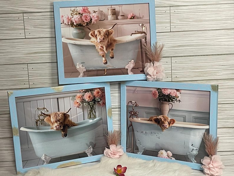 May include: Three framed prints of Highland cows in a bathtub with pink flowers. The frames are light blue with gold accents.