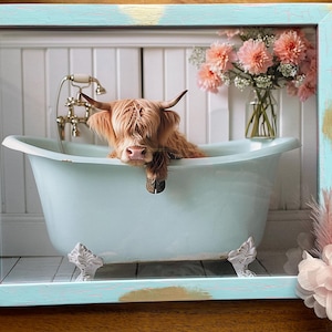 May include: A Highland cow takes a bath in a light blue bathtub with white feet. The cow is brown and white and has its head resting on the edge of the tub. The bathtub is in a white bathroom with white tile walls and a white tiled floor. There are pink flowers in a vase in the background.