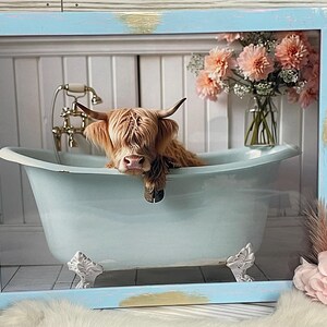 May include: A Highland cow with brown fur is taking a bath in a light blue clawfoot bathtub. The cow is looking at the camera with its head resting on the edge of the tub. The bathtub is in a white bathroom with a white tiled floor. There are pink flowers in a vase in the background.