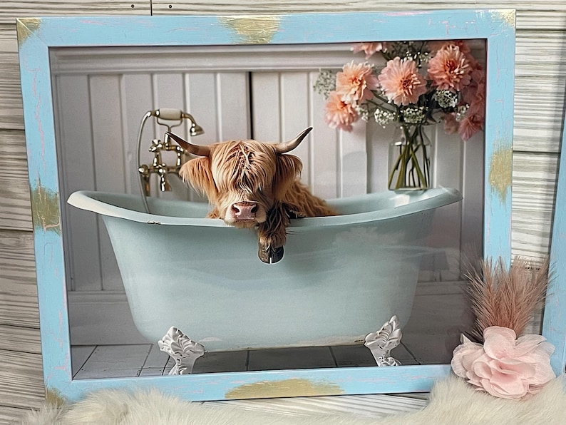 May include: A Highland cow with brown fur is taking a bath in a light blue clawfoot bathtub. The cow is looking at the camera with its head resting on the edge of the tub. The bathtub is in a white bathroom with a white tiled floor. There are pink flowers in a vase in the background.