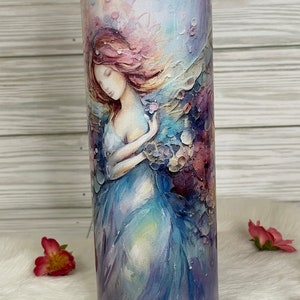 May include: A stainless steel tumbler featuring a watercolor painting of a woman in a flowing blue dress. The artwork has soft pastel colors, including pink, purple, and blue. The tumbler is cylindrical and has a clear lid.