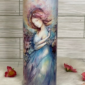 May include: A stainless steel tumbler featuring a watercolor painting of a woman in a flowing blue dress, surrounded by flowers. The artwork has soft pastel colors, with pink, purple, and blue hues. The tumbler is cylindrical and has a clear lid.