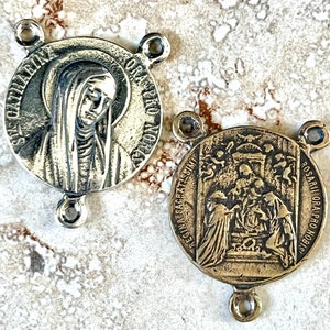 May include: Two silver-toned metal medallions with religious imagery. The left medallion features a depiction of Saint Catherine of Siena with the text "S. CATHERINA DA SIENA" around the edge. The right medallion features a depiction of the Virgin Mary with the text "REGINA SACRATISSIMA ROSARII ORA PRO NOBIS" around the edge.