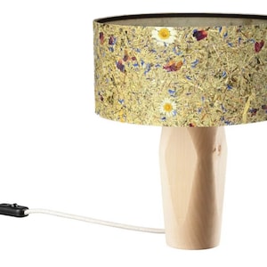 Könnte beinhalten: Eine Tischlampe aus Holz mit einem zylindrischen Lampenschirm, der mit einem floralen Druck aus getrockneten Blumen und Blättern auf beigefarbenem Hintergrund verziert ist.