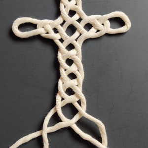 May include: A white rope is woven into a cross shape. The rope is tied in a complex knot pattern.