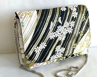 Bolso de mano blanco y negro con rayas doradas y pequeño estampado floral