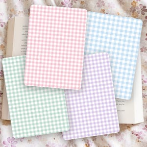 May include: Four rectangular cards with rounded corners, each displaying a gingham pattern in pastel shades: pink, blue, green, and purple. The cards are placed on an open book, creating a soft, inviting aesthetic.