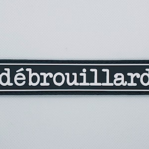 May include: Black and white patch with the text "débrouillard" in white lettering.