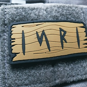 May include: A brown and black patch with the word "IMRI" written in black letters on a wood grain background.