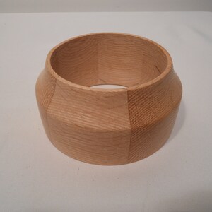 May include: A light brown wooden bowl with a rounded bottom and a slightly flared top. The bowl is made of multiple pieces of wood that have been joined together.