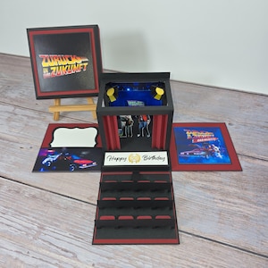 Könnte beinhalten: Eine Pop-up-Geburtstagskarte zum Thema Zurück in die Zukunft. Die Karte zeigt eine Bühne mit roten Vorhängen, einen DeLorean und den Text "Happy 50 Birthday". Die Karte ist schwarz und rot mit dem Filmtitel auf Deutsch.