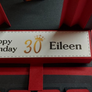 Puede incluir: Tarjeta de cumplea&ntilde;os hecha a mano con un dise&ntilde;o rojo y negro. La tarjeta presenta el texto "Happy Birthday 30 Eileen" en letras doradas y negras. La tarjeta tiene un dise&ntilde;o desplegable y una corona decorativa.