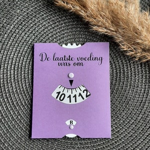 May include: A purple card with the text "De laatste voeding was om" and a clock face with a black hand pointing to the number 11.