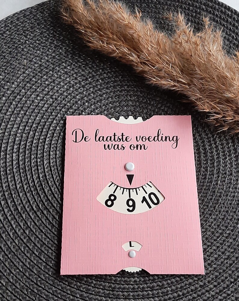 May include: A pink card with the text "De laatste voeding was om" and a dial with numbers 8, 9, and 10. The dial has a white arrow pointing to the number 9.