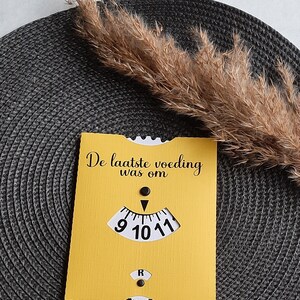 May include: A yellow card with the text "De laatste voeding was om" and a clock face with a black hand pointing to the number 10. The clock face is white with black numbers 9, 10, and 11.