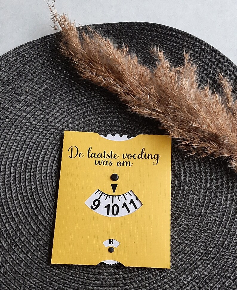 May include: A yellow card with the text "De laatste voeding was om" and a clock face with a black hand pointing to the number 10. The clock face is white with black numbers 9, 10, and 11.