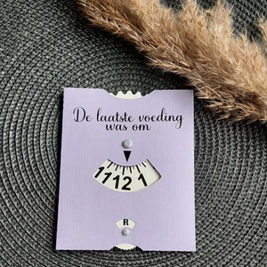 May include: A purple card with the text "De laatste voeding was om" and a dial with numbers 1, 12, 11, and 7.