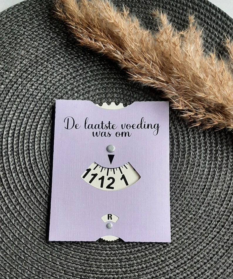 May include: A purple card with the text "De laatste voeding was om" and a dial with numbers 1, 12, 11, and 7.