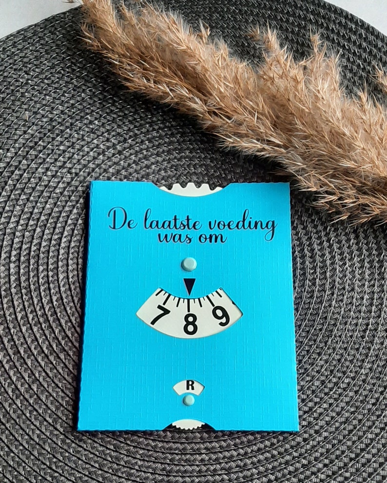 May include: A blue card with the text "De laatste voeding was om" and a white dial with black numbers 7, 8, and 9. The dial has a black arrow pointing to the number 8.