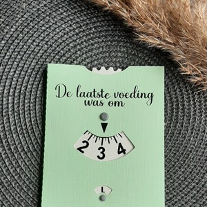 May include: A light green card with the text "De laatste voeding was om" and a white dial with numbers 2, 3, and 4. The dial has a black arrow pointing to the number 3.