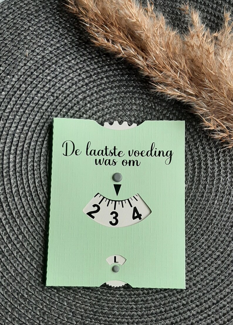 May include: A light green card with the text "De laatste voeding was om" and a white dial with numbers 2, 3, and 4. The dial has a black arrow pointing to the number 3.